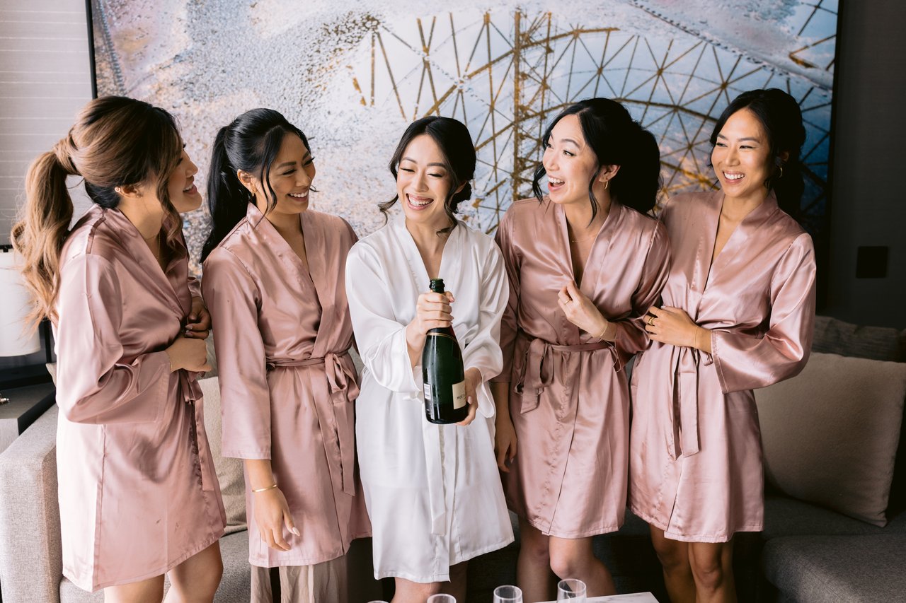 The bridesmaids in pink robes, champagne before the dress