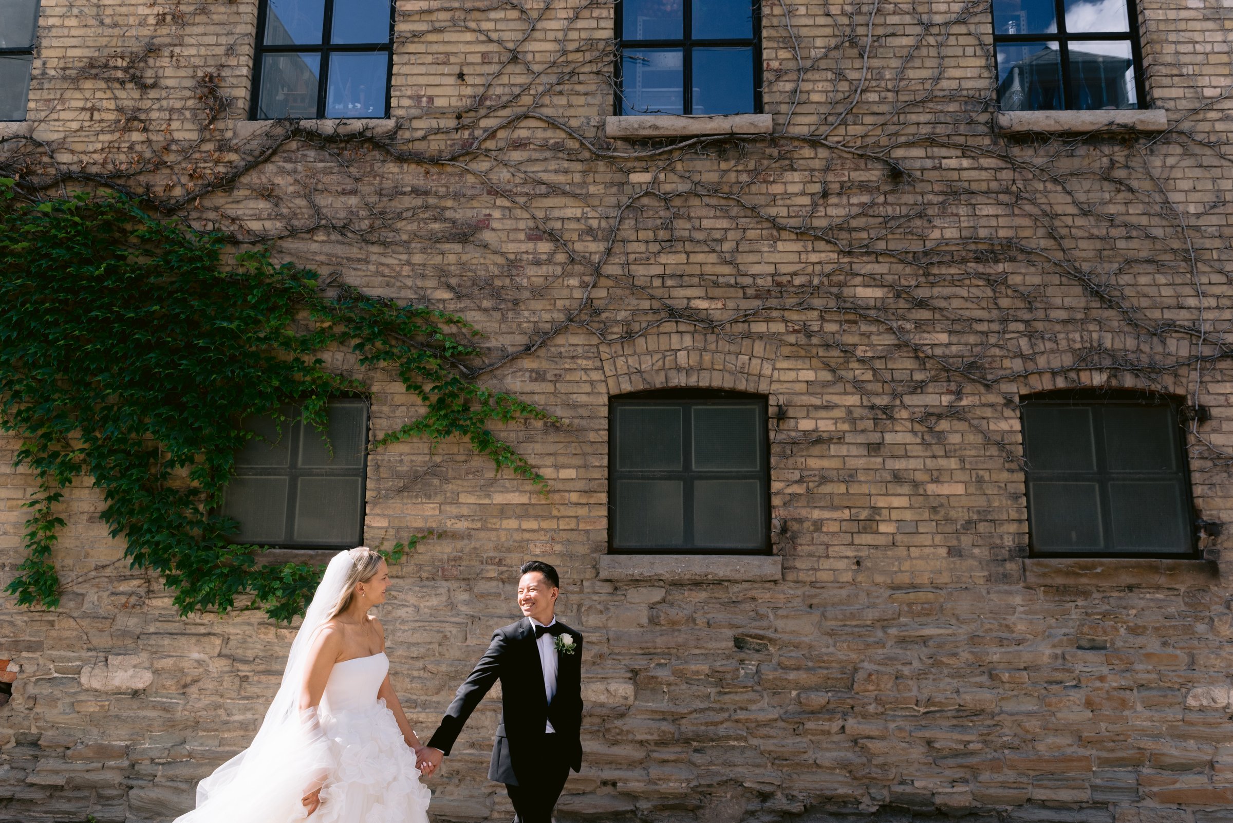 Magda and Terrence walking the ivy-covered Distillery brick, the dress trailing