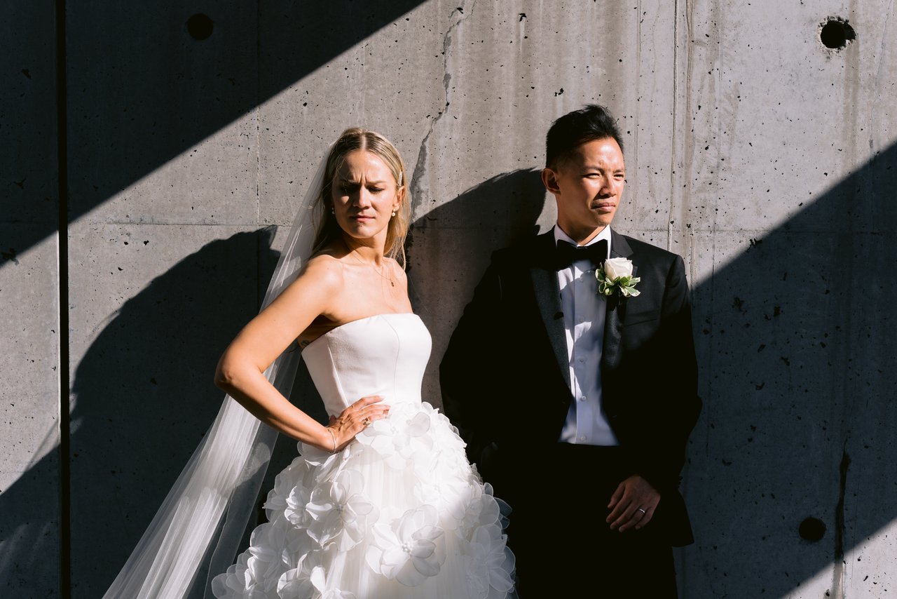 Magda and Terrence against a sunlit concrete wall, a hard diagonal shadow across it