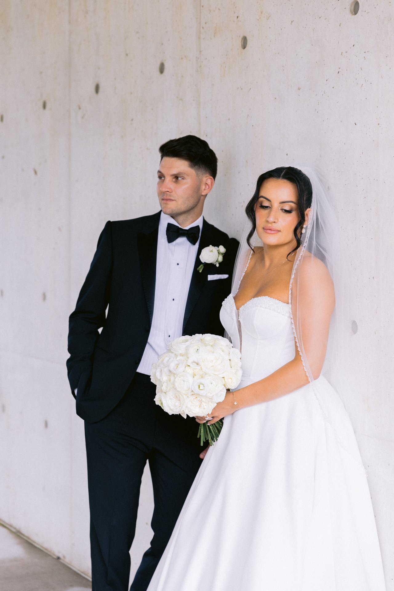 Against the concrete wall, bouquet in hand