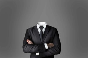 En huvudlös figur i kostym med armarna i kors framför en grå bakgrund.