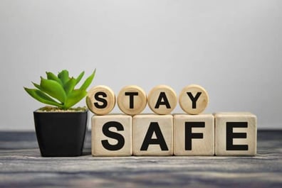 des blocs de bois empilés sur un plan de travail lisant le texte "restez en sécurité", avec une petite plante à gauche