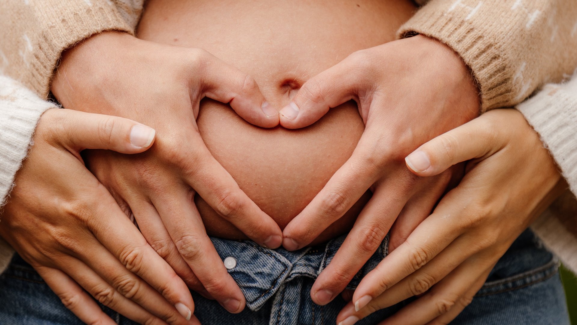 Gravid mage med to par hender formet som et hjerte