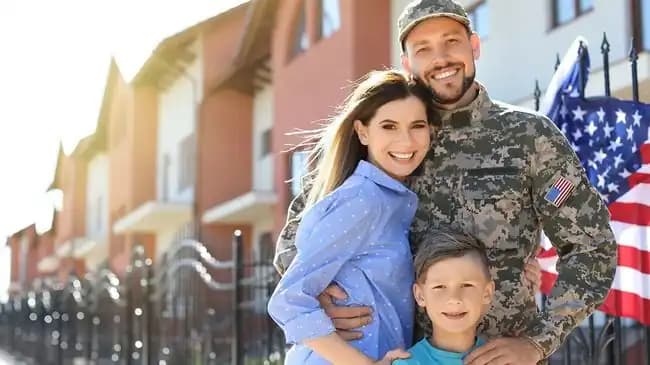 Service member standing with his family outside a row of homes