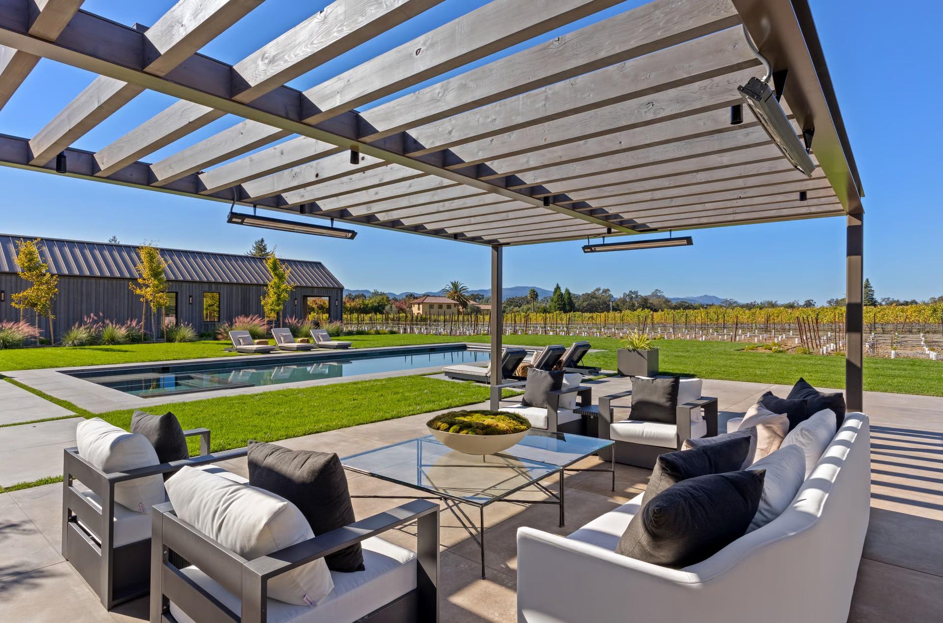 Covered outdoor lounge overlooking a swimming pool and vineyard
