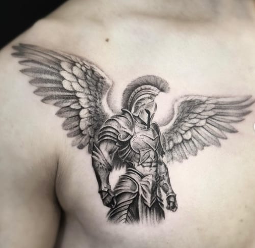 A black and grey realism tattoo of an armored angel with detailed wings on the chest — by Jian Liang, los angeles