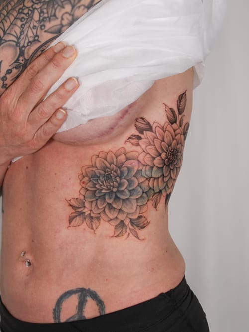 A delicate and realistic flower bouquet tattoo on the rib, featuring detailed shading and a mix of colors — by Melanie Benoit, los angeles