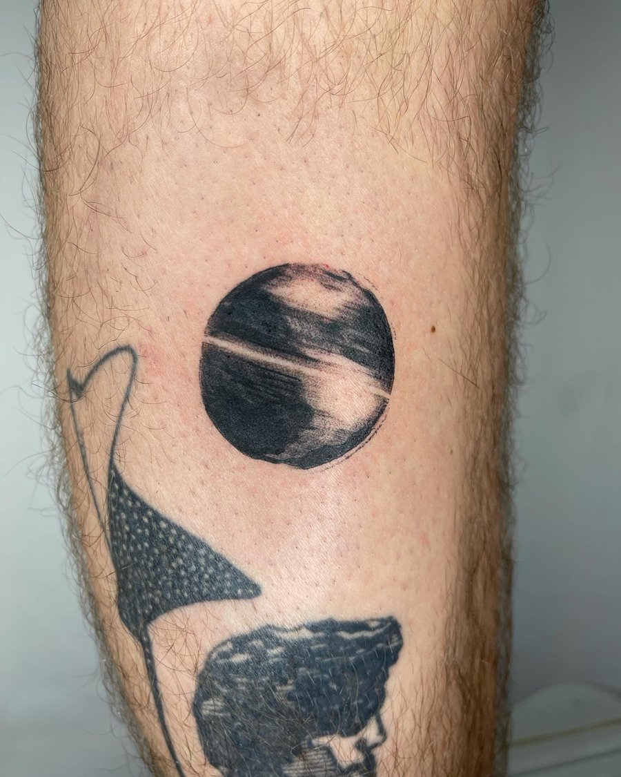 A minimalist black and grey planet tattoo on the leg, featuring a simple celestial design — by Level tattoo, los angeles