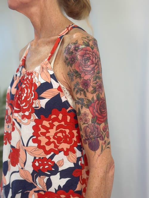 A colorful floral bouquet tattoo on the upper arm featuring roses and other flowers in a realistic style — by Melanie Benoit, los angeles