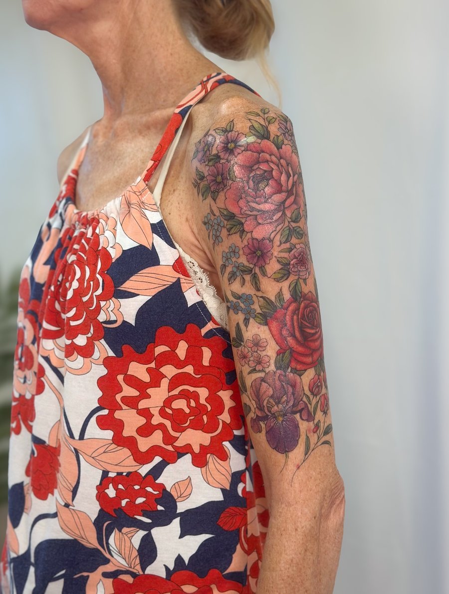 A colorful floral bouquet tattoo on the upper arm featuring roses and other flowers in a realistic style — by Melanie Benoit, los angeles