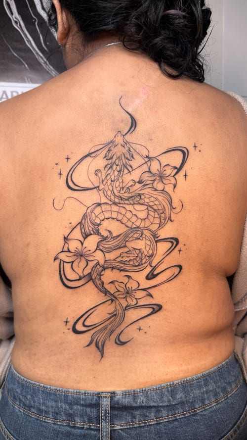 A black and grey linework tattoo of a dragon intertwined with flowers on the back, featuring elegant curves and fine details — by NJ TATTOOZ, los angeles