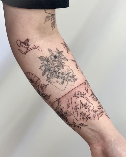 A delicate black and grey floral arrangement with hands on the forearm, featuring fine line botanical details — by Melanie Benoit, los angeles