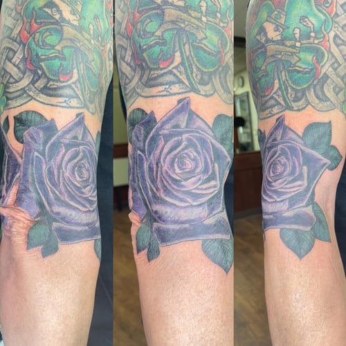 A bold, colorful rose tattoo on the forearm with realistic shading and vibrant purple hues — by Sandra Price, los angeles