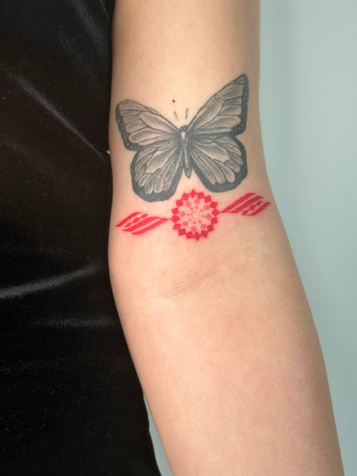 A minimalist black and grey butterfly tattoo on the forearm, accented with a red geometric design below it — by Brian Kies, los angeles