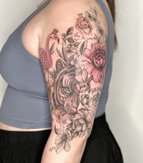 A mixed color and black and grey tattoo of a tiger surrounded by flowers on the upper arm, featuring illustrative and delicate details — by Melanie Benoit, los angeles