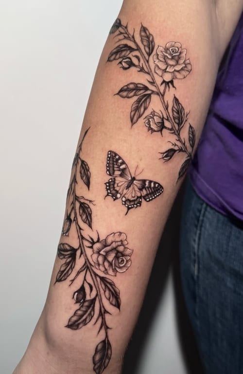 A black and grey fine line tattoo on the forearm featuring roses and a butterfly with intricate details — by Shelby Bianco, los angeles