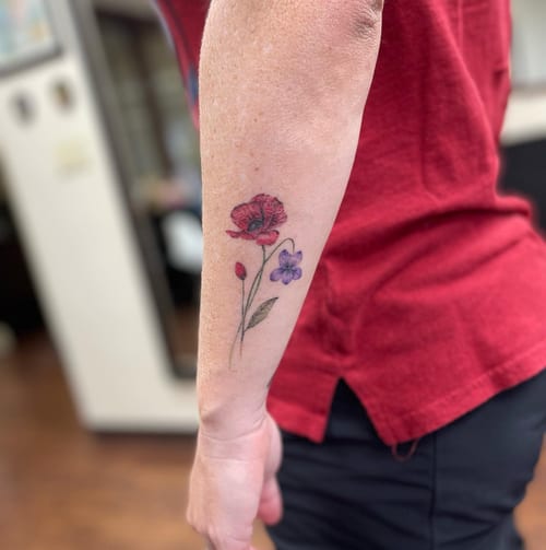 A delicate fine line flower bouquet tattoo on the forearm featuring colorful flowers in a botanical style — by Sandra Price, los angeles