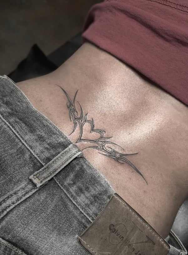 A black and grey tribal tattoo on the lower back featuring a heart with intricate linework and sharp edges — by Shelby Bianco, ventura, ca