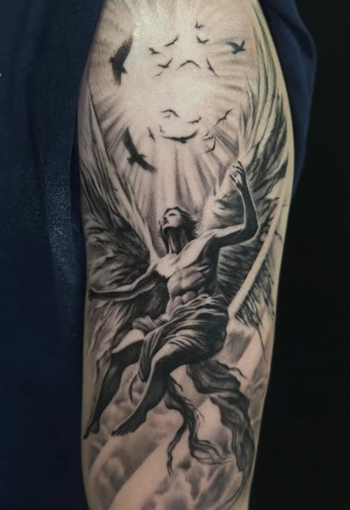 A black and grey realism tattoo of an angel with wings surrounded by birds on the upper arm, featuring detailed shading and dynamic movement — by Jian Liang, los angeles