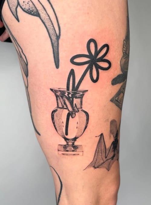 A minimalist black and grey tattoo of a simple flower in a vase on the thigh, featuring clean linework — by Level tattoo, los angeles