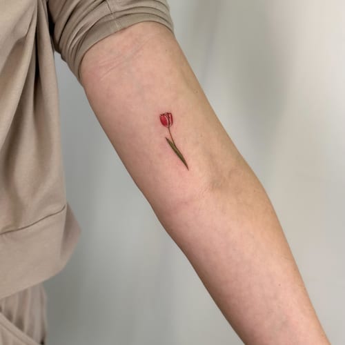 A small, delicate color tulip tattoo on the forearm in a minimalist style — by Melanie Benoit, los angeles