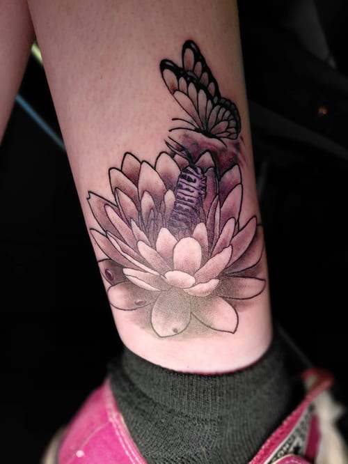 A black and grey fine line tattoo of a lotus flower with a butterfly on the calf, featuring delicate linework and shading — by anoetic.designs.ultd, los angeles