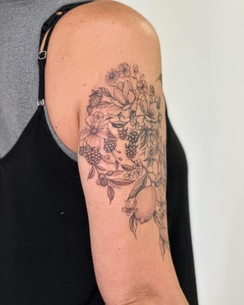 A delicate black and grey floral and fruit bouquet tattoo on the upper arm with fine line details — by Melanie Benoit, los angeles