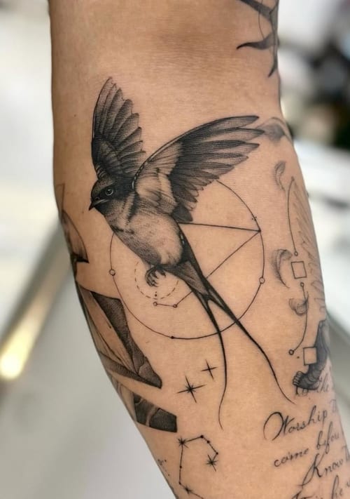 A black and grey tattoo of a bird with outstretched wings, surrounded by geometric shapes and lines on the forearm — by otaybeatdown, los angeles