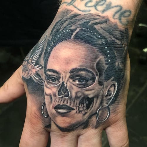 A realistic black and grey tattoo of a woman's portrait with a skull overlay on the hand, featuring detailed shading and intricate design — by Johnny Ayala, los angeles