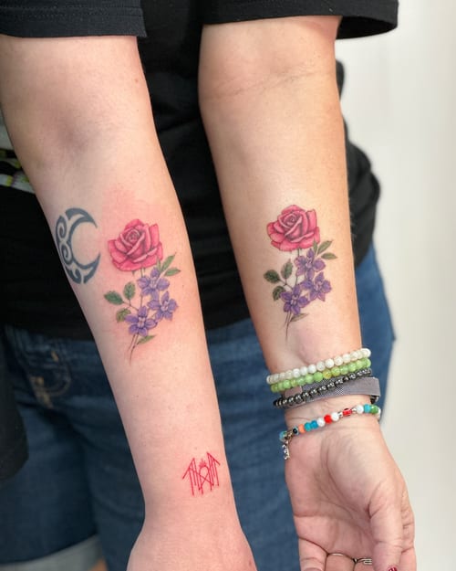 A colorful floral tattoo on the forearm featuring a rose and purple flowers in a delicate fine line style — by Melanie Benoit, los angeles