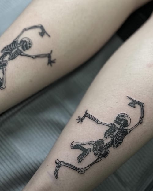 A fine line black and grey tattoo of dancing skeletons on the leg — by Maddie Ramirez, los angeles