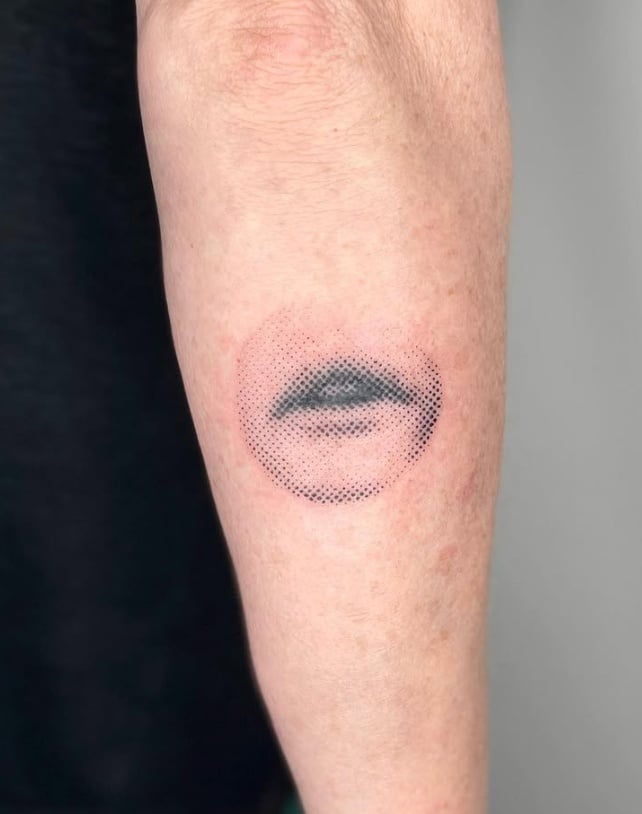 A minimalist dotwork tattoo of a partial face on the forearm, featuring a black and grey color scheme with a focus on the eye and lips — by Level tattoo, los angeles