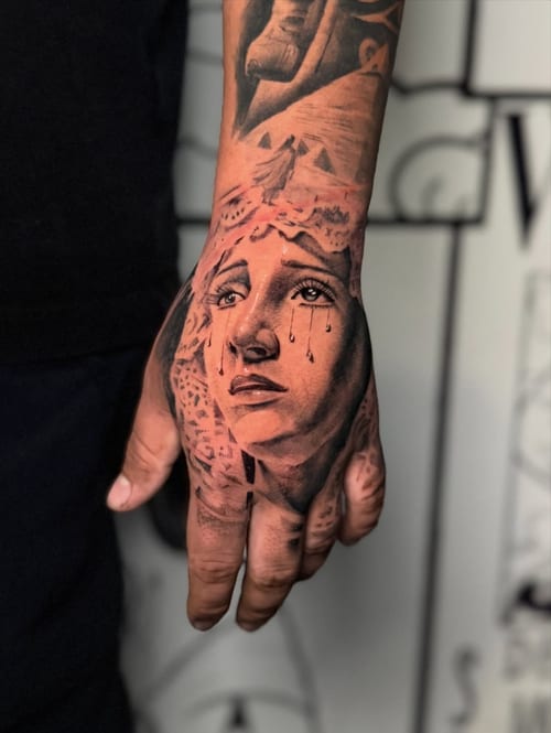 A realistic black and grey portrait of a crying woman on the hand, featuring detailed shading and ornate elements — by zealous, los angeles