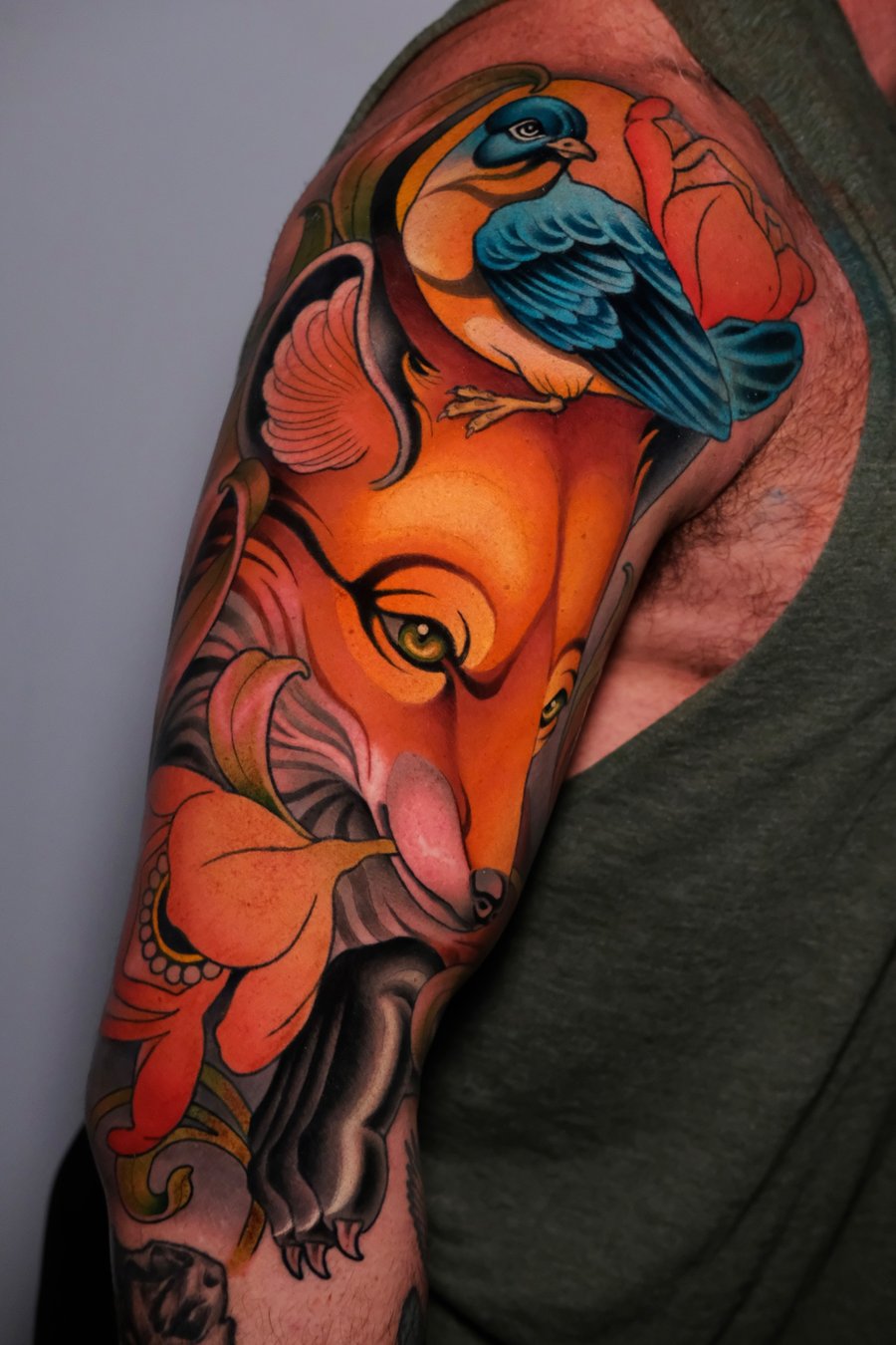 A vibrant neo-traditional tattoo on the upper arm featuring a fox and a bird surrounded by floral elements, with bold outlines and rich colors — by Gabe Motta, los angeles