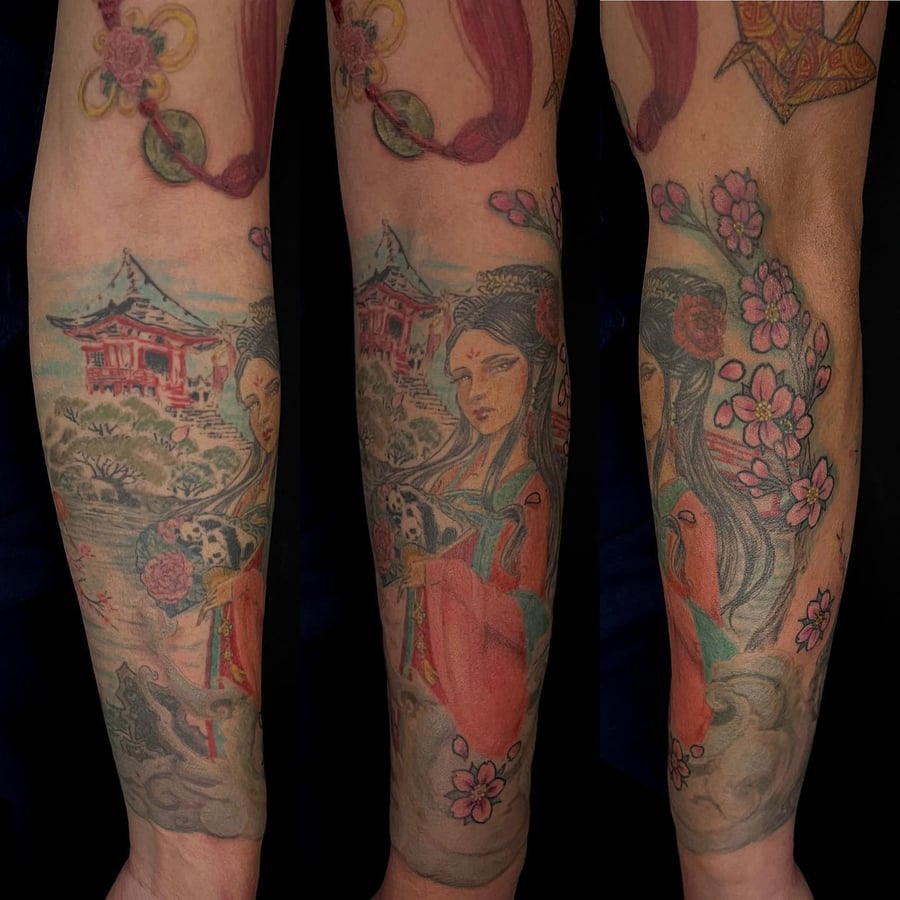 A colorful Japanese-style tattoo on the forearm depicting a woman in traditional attire surrounded by cherry blossoms and a scenic background — by Sandra Price, los angeles