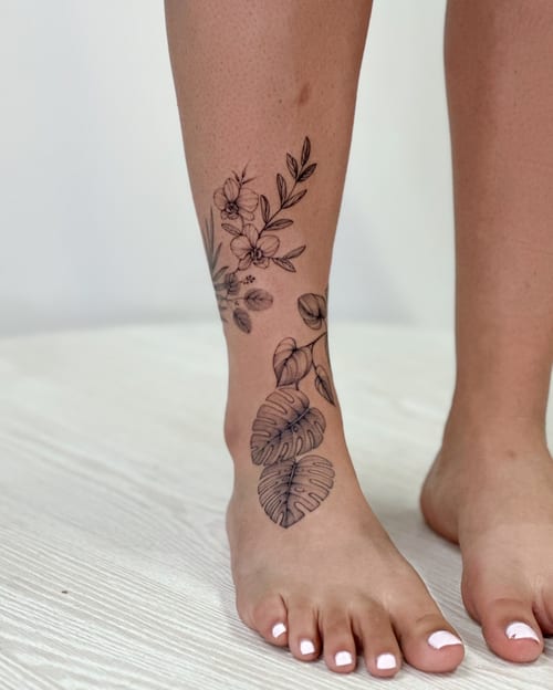 A delicate black and grey fine line tattoo of flowers and leaves on the leg, showcasing a minimalist botanical design — by Melanie Benoit, los angeles