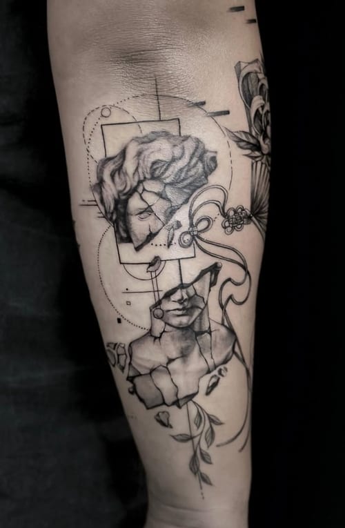 A black and grey surrealistic tattoo on the forearm featuring fragmented classical sculptures of faces with floral and geometric elements — by Jian Liang, los angeles
