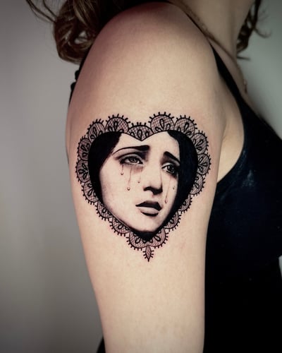 A black and grey portrait of a woman with tears, framed by an ornamental heart design on the upper arm — by emily, los angeles