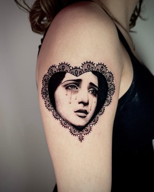 A black and grey portrait of a woman with tears, framed by an ornamental heart design on the upper arm — by emily, los angeles