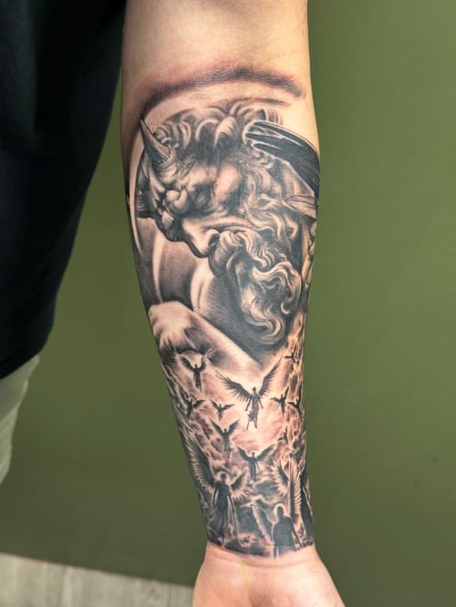 A detailed black and grey realism tattoo of an angel with wings on the forearm, featuring intricate shading and dynamic composition — by Humilde tattoos, los angeles