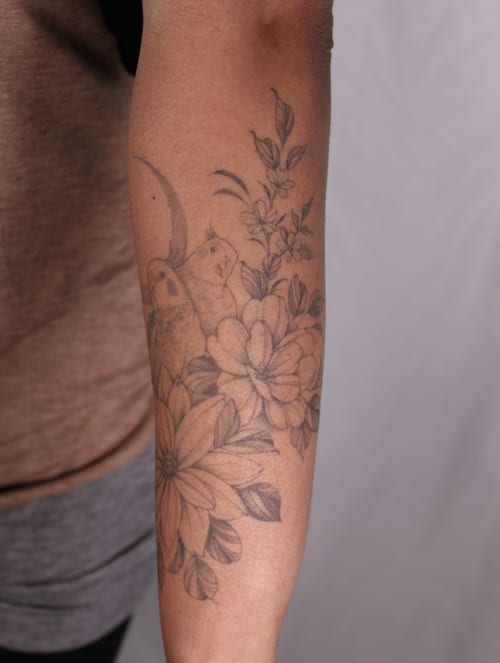 A delicate black and grey tattoo of flowers and birds on the forearm, featuring intricate floral details — by Melanie Benoit, los angeles