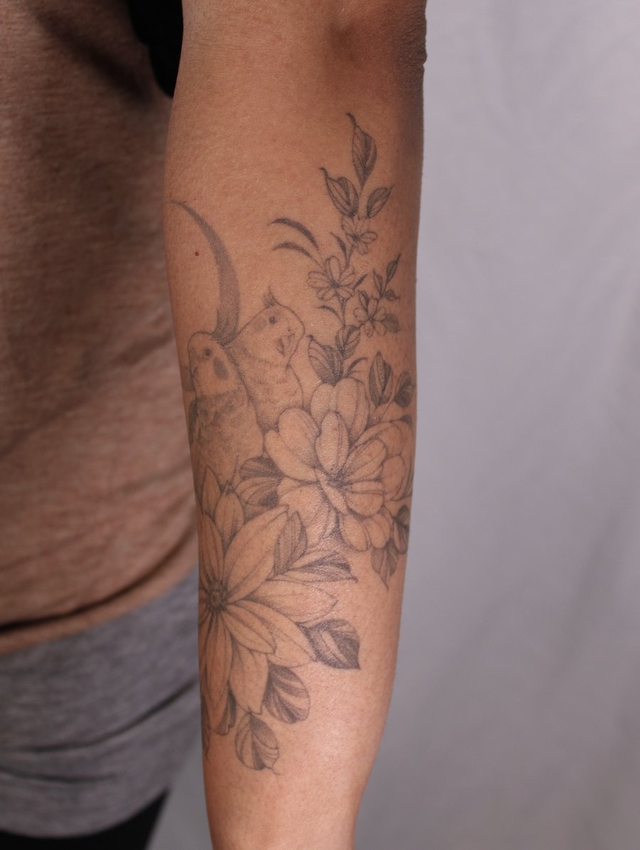 A delicate black and grey tattoo of flowers and birds on the forearm, featuring intricate floral details — by Melanie Benoit, los angeles