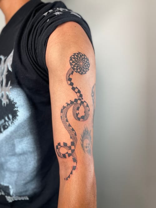 A geometric black and grey snake tattoo on the upper arm, featuring intricate patterns and bold lines — by Brian Kies, los angeles