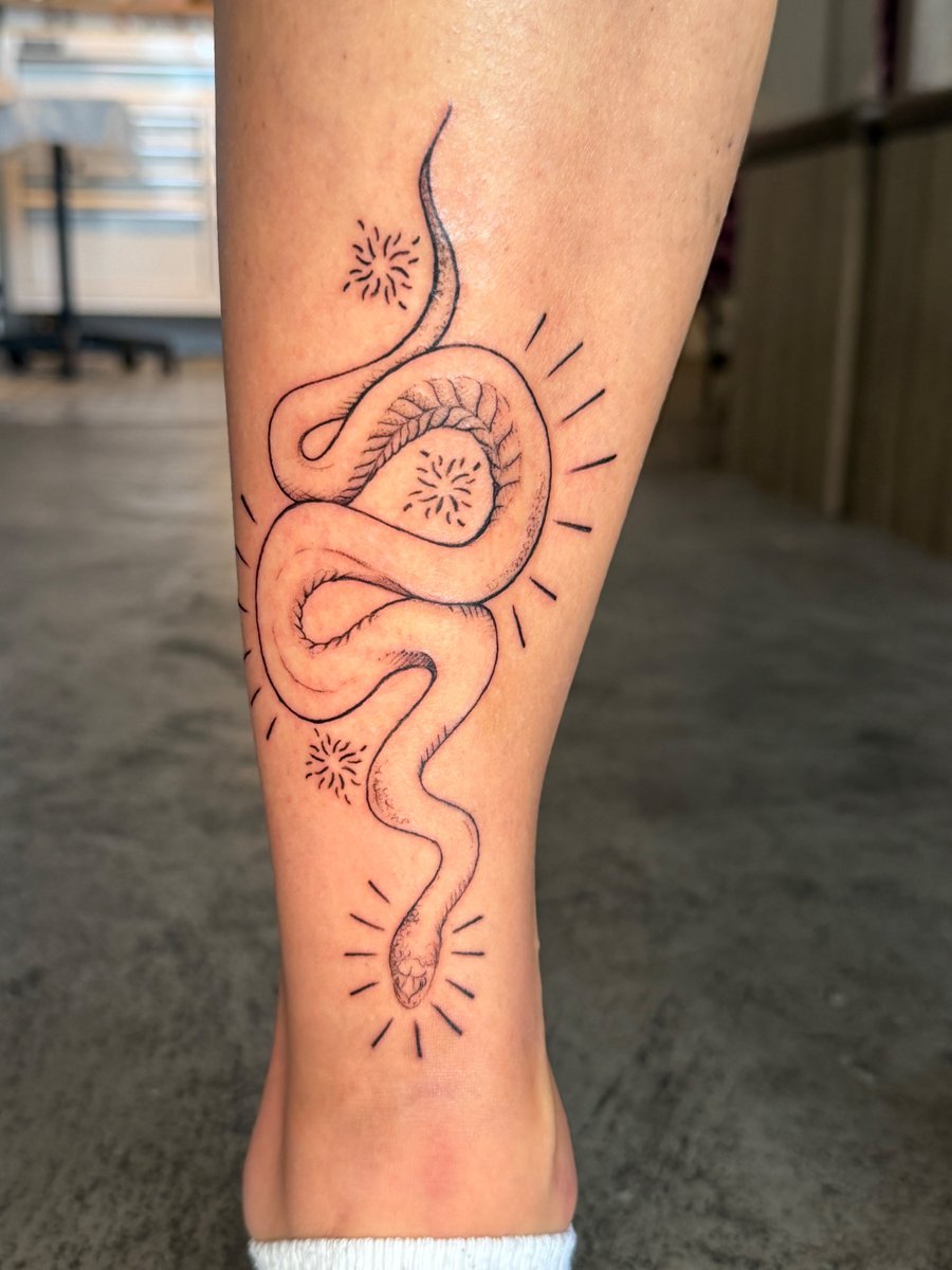 A minimalist fine line snake tattoo on the calf, featuring delicate black and grey linework — by Kiera Garvin, los angeles