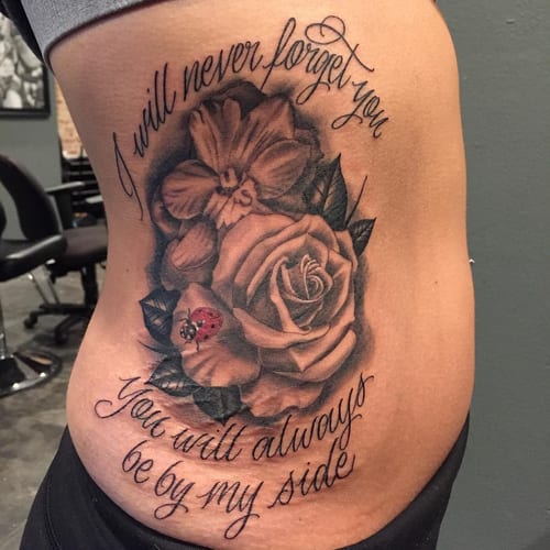 A black and grey rose bouquet with script lettering on the rib, featuring realistic shading and a memorial quote — by Johnny Ayala, los angeles