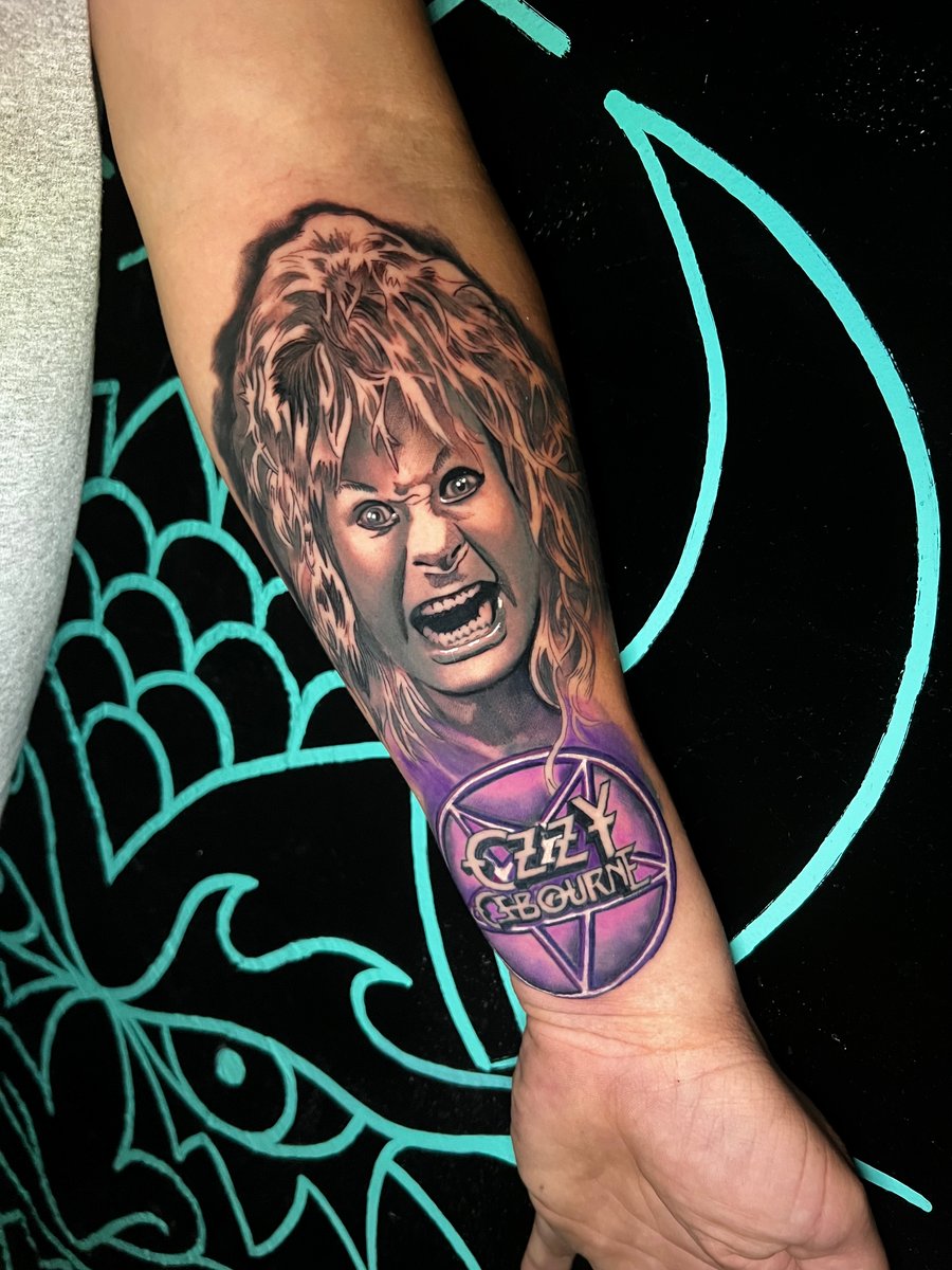 A colorful portrait tattoo on the forearm featuring a detailed depiction of a person's face with vibrant purple and skin tones — by Josue Bravo, los angeles