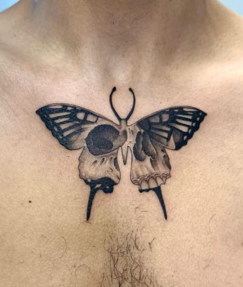 A black and grey surrealistic tattoo on the chest, depicting a butterfly with skulls integrated into its wings — by otaybeatdown, los angeles
