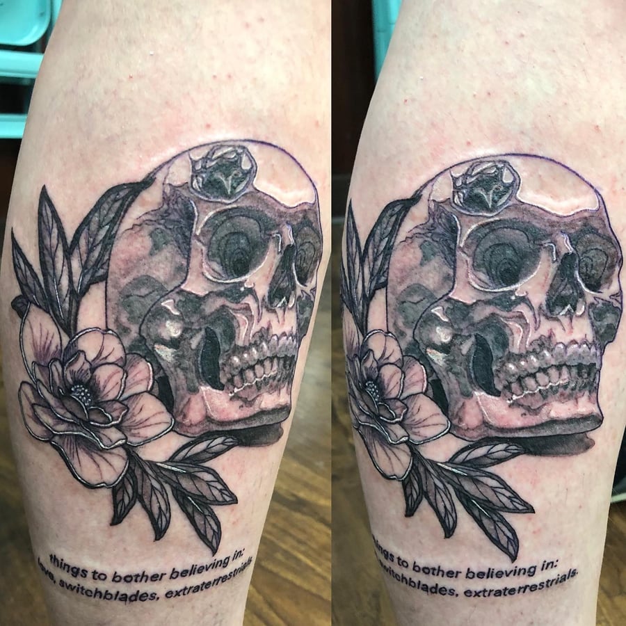 A bold black and grey skull with flowers tattoo on the calf, featuring a neo-traditional style with graphic elements — by Sandra Price, los angeles
