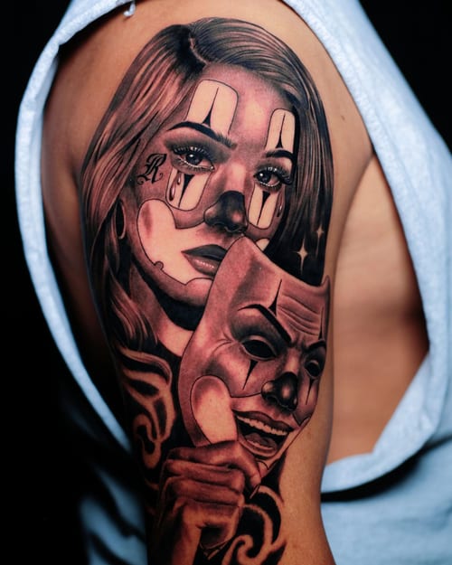 A black and grey tattoo of a woman with clown makeup holding a mask on the upper arm, done in a realistic Chicano style — by Johnny Ayala, los angeles