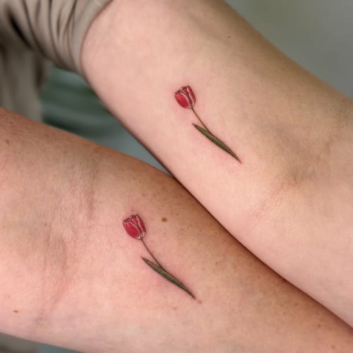 A delicate and minimalist tulip tattoo in color on the forearm, featuring fine line work — by Melanie Benoit, los angeles